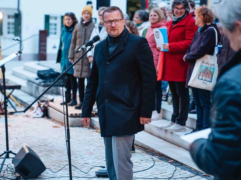 Bürgermeister Stefan Wörner steht auf dem Marktplatz vor einem Mikrofon und spricht. Hinter ihm hat sich ein Chor aufgestellt.