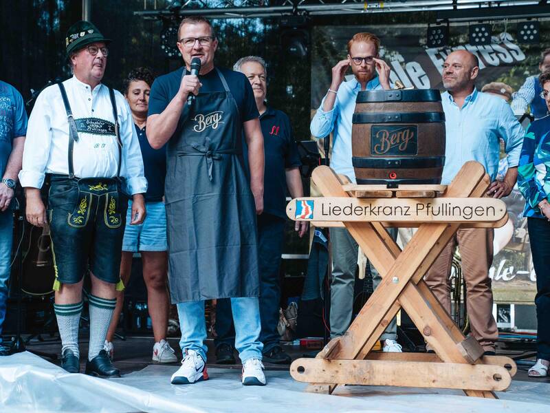 Bürgermeister Stefan Wörner steht links neben einem Bierfass und spricht in ein Mikrofon. Um ihn herum stehen mehrere Menschen.