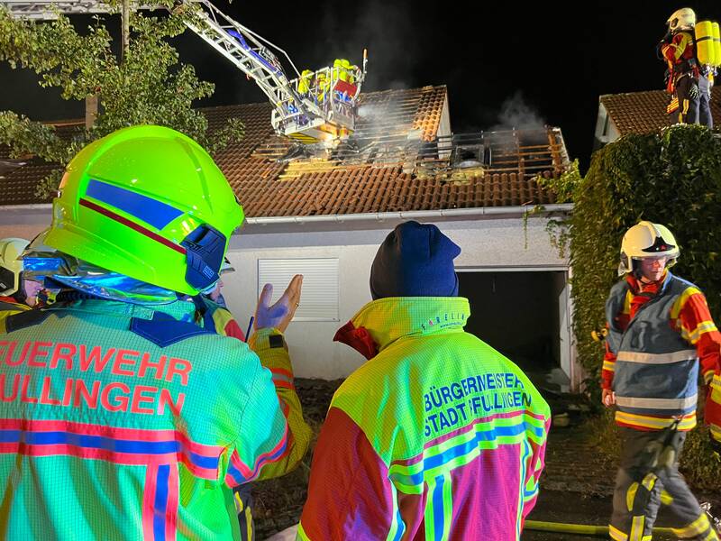 Zu sehen sind von hinten Bürgermeister Stefan Wörner, wie er von Feuerwehrkommandant DIetmar Rall, der links neben ihm steht, etwas erläutert bekommt. Im Hintergrund ist ein Gebäude zu sehen, dessen Dach durch einen Brand zerstört ist.