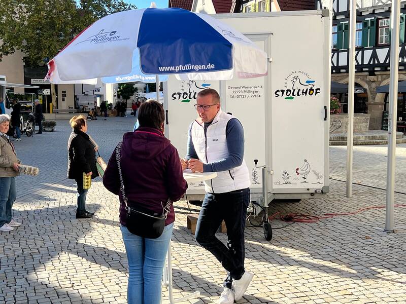 Bürgermeister Stefan Wörner steht auf dem Marktplatz an einem Stehtisch mit Schirm und spricht mit einer Frau.